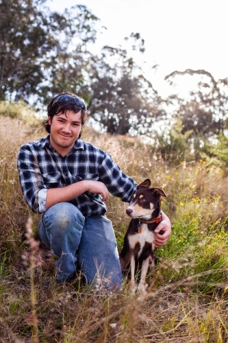Portrait of young man in his twenties resting with kelpie puppy in grass - Australian Stock Image