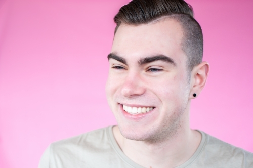 Portrait of young man laughing on plain pink background