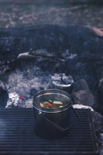 Pot of vegetable soup cooking on grill on campfire coals - Australian Stock Image
