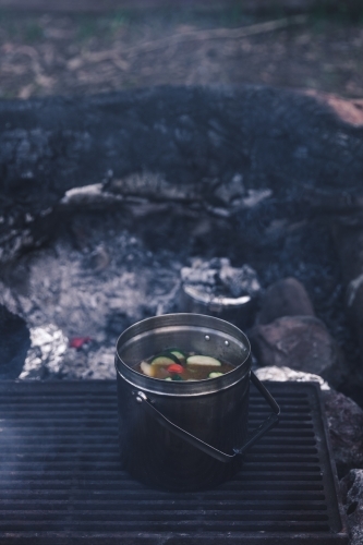 Pot of vegetable soup cooking on grill on campfire coals