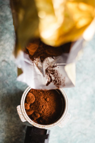Pouring fresh ground coffee from a bag into an espresso portafilter - Australian Stock Image