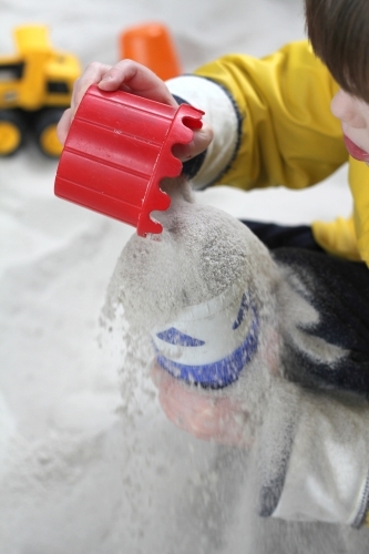 pouring sand between cups in sandpit - Australian Stock Image