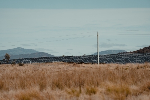 Power lines in front of solar farm panels for renewable energy with mountains in the background. - Australian Stock Image