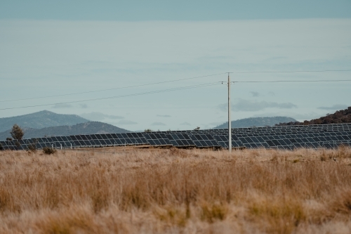 Power lines in front of solar farm panels for renewable energy with mountains in the background.