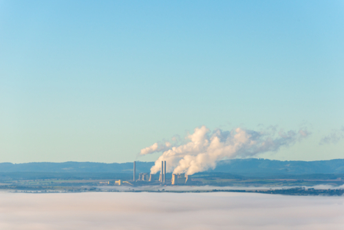 Power station chimneys emitting steam above low morning fog in rural landscape. - Australian Stock Image