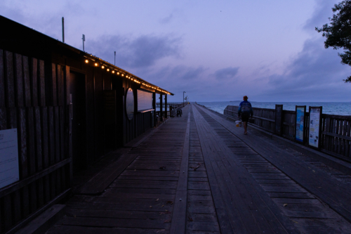 pre-dawn jetty with festoon lights and someone walking out to fish - Australian Stock Image