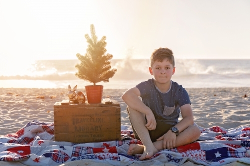 Pre Teen Boy Sitting In a Christmas Themed Setting At The Beach At Sunset - Australian Stock Image
