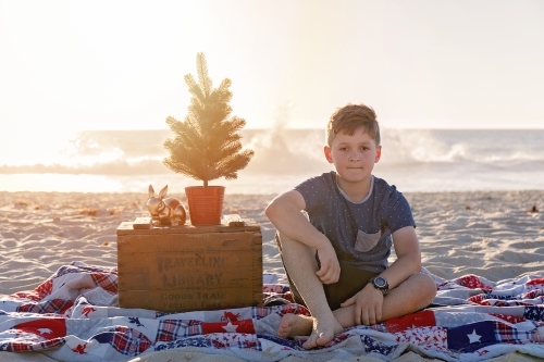 Pre Teen Boy Sitting In a Christmas Themed Setting At The Beach At Sunset