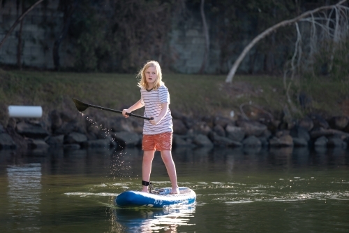 Pre-teen boy stand up paddle boarding on lake - Australian Stock Image