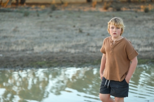 Pre-teen boy standing near creek in dry remote bush setting - Australian Stock Image