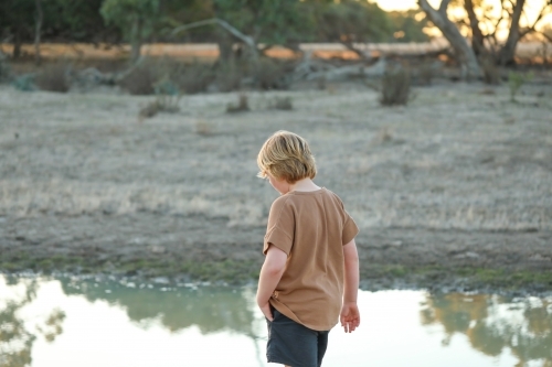 Pre-teen boy walking along creek in dry remote bush setting - Australian Stock Image
