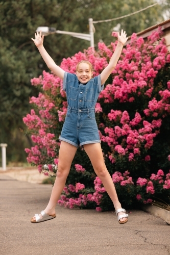 Pre-teen girl jumping in front of vibrant pink bougainvillea bush - Australian Stock Image