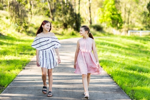Pre-teen sisters walking along a footpath through a park in summer
