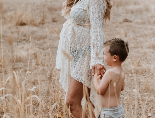 Pregnant mother walking with son through brown grass - Australian Stock Image