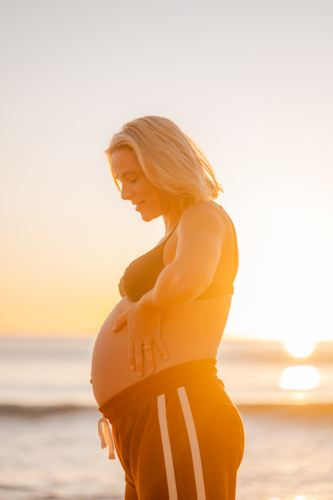 pregnant woman at Manly Beach during sunrise showing baby bump - Australian Stock Image