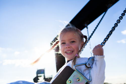 Preschool aged child swinging on swing at playground in early morning having fun by herself - Australian Stock Image