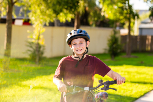 Preteen boy smiling in helmet beside his bike on warm afternoon at park - Australian Stock Image