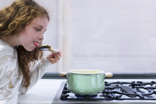 Preteen girl helping to cook over a saucepan on a stove in the kitchen