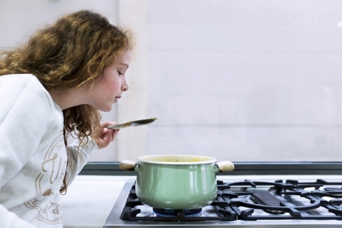 Preteen girl helping to cook over a saucepan on a stove in the kitchen