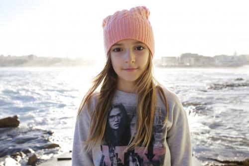 Pretty young girl wearing a beanie standing by the ocean - Australian Stock Image