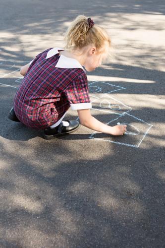 Primary school aged girl in uniform drawing chalk on asphalt - Australian Stock Image