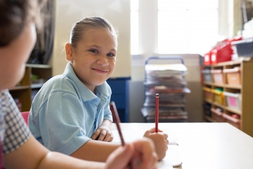 Primary school girl sitting in a classroom smiling - Australian Stock Image