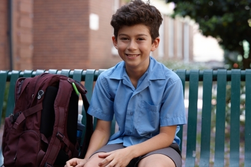 Primary school student at sitting on the bench with backpack smiling - Australian Stock Image