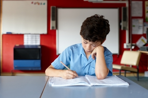 Primary school student in classroom working on homework - Australian Stock Image
