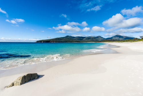 Pristine white sand beach with turquoise water and distant mountains - Australian Stock Image