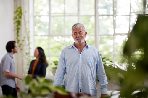Professional businessman standing, thinking in an open plan office studio - Australian Stock Image