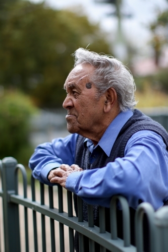 Profile of male Aboriginal elder leaning against a fence