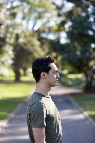 Profile of young man with dark hair standing outside at park - Australian Stock Image