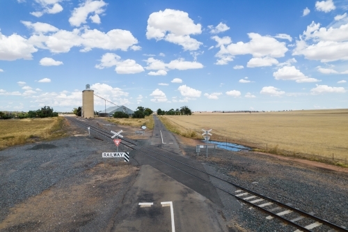 Railway crossing in the middle of fields with the silos in the distance. - Australian Stock Image