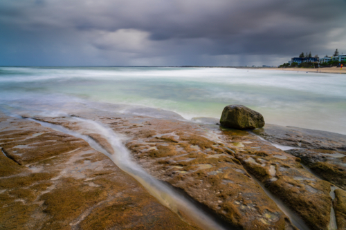 Rain falling from dark storm clouds over rockpools on Kings Beach at Caloundra in Queensland - Australian Stock Image