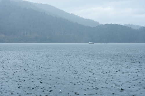 Rain on lake with boat and hills in distance - Australian Stock Image