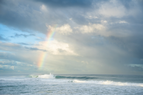 Rainbow forming over crashing ocean waves at Scarborough Beach, Perth, Western Australia - Australian Stock Image