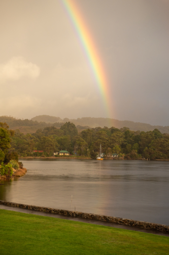 Rainbow over harbour waters with yacht on calm waters - Australian Stock Image