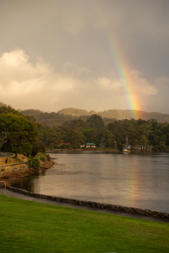 Rainbow over harbour waters with yacht on calm waters - Australian Stock Image