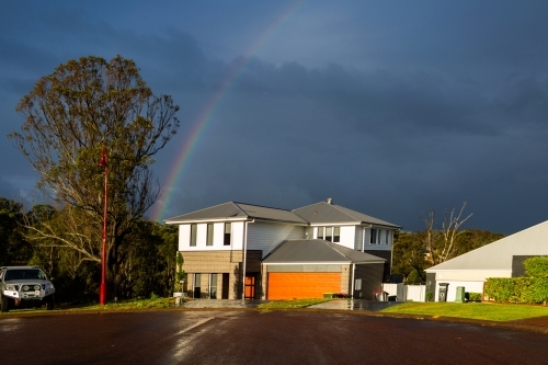 Rainbow over home at the end of a cul-de-sac with dark storm clouds behind