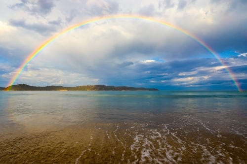Rainbow over ocean and sandy beach - Australian Stock Image