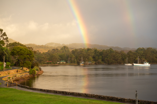 Rainbows over harbour waters with yacht on calm waters - Australian Stock Image