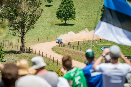 Rally car taking a corner from afar with crowd in the foreground