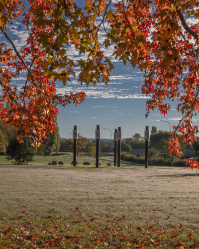 Red autumn leaves framing a country scene under blue skies, a park and an art sculpture - Australian Stock Image