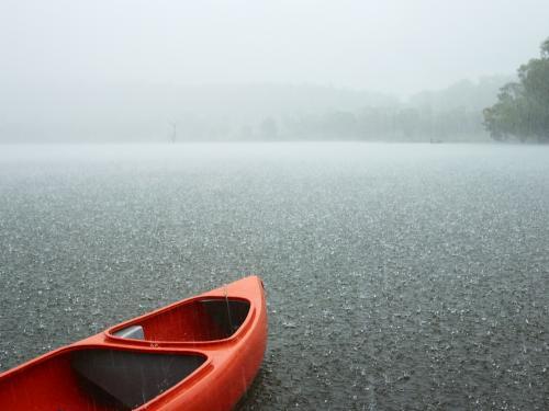 Red canoe sits idle on grey rainswept lake.