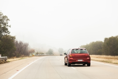 Red car overtaking in the right hand lane in foggy conditions