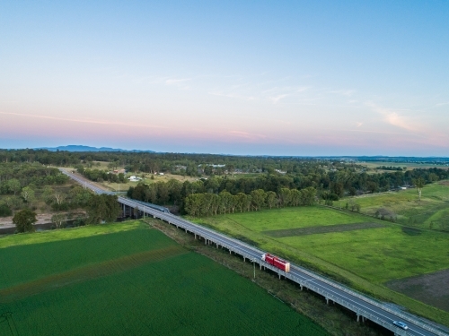 Red cattle truck on bridge travelling through green farmland in country - Australian Stock Image