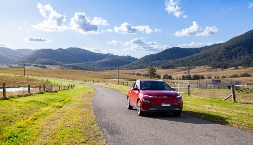 Red electric vehicle car driving down rural country road on sunlit day