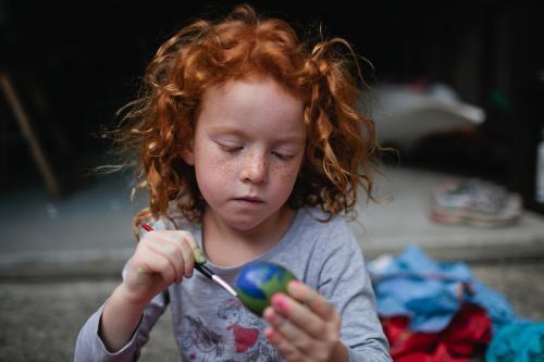 Red haired girl painting easter eggs