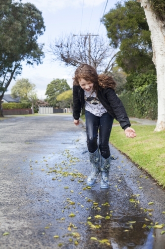 Red haired girl splashing in puddles in gumboots on a rainy winter day. - Australian Stock Image
