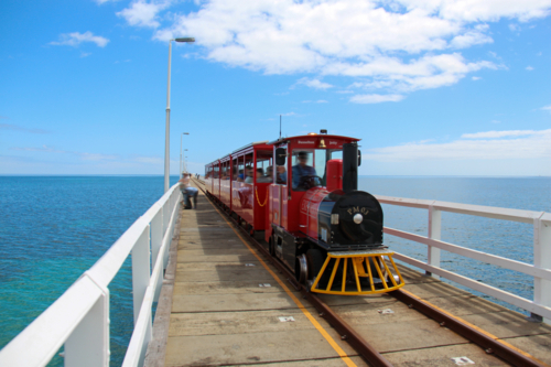 Red passenger train on Busselton jetty above ocean - Australian Stock Image